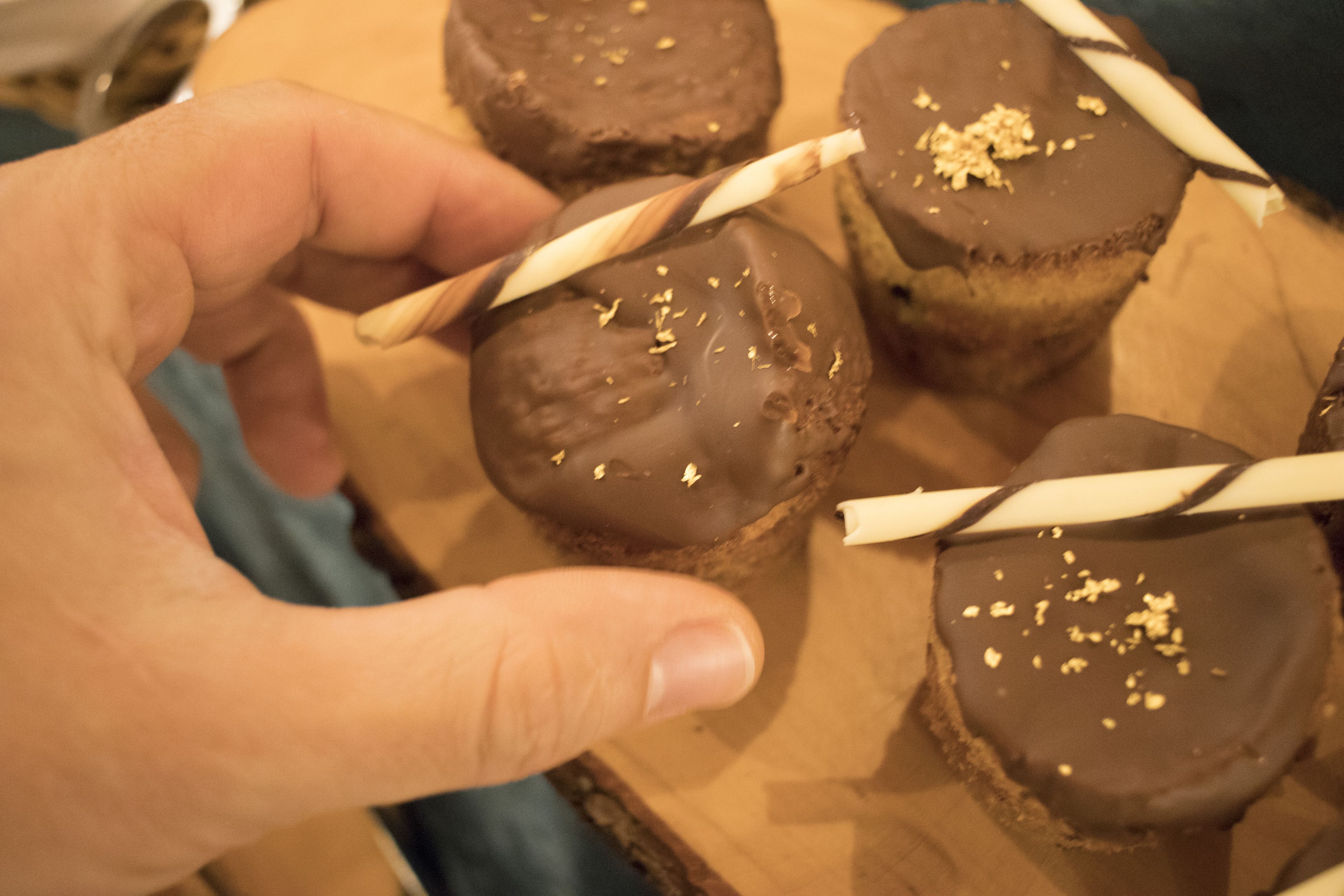 Una mano sostiene un dulce bañado en chocolate con una pajita a rayas sobre una tabla de madera.