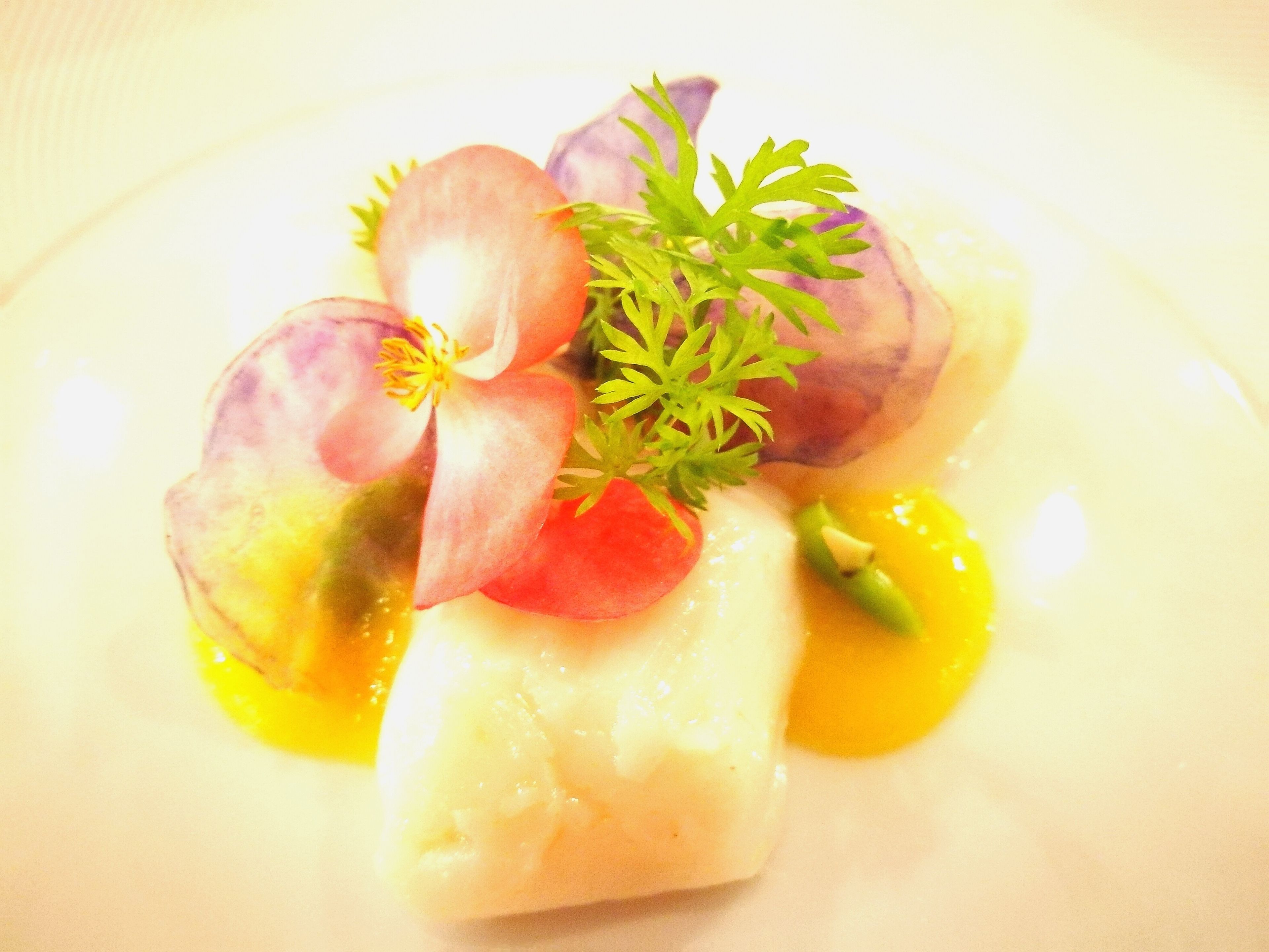A dish with a white base, possibly fish, topped with slices of red and purple vegetables, garnished with green herbs.