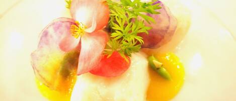 A dish with a white base, possibly fish, topped with slices of red and purple vegetables, garnished with green herbs.