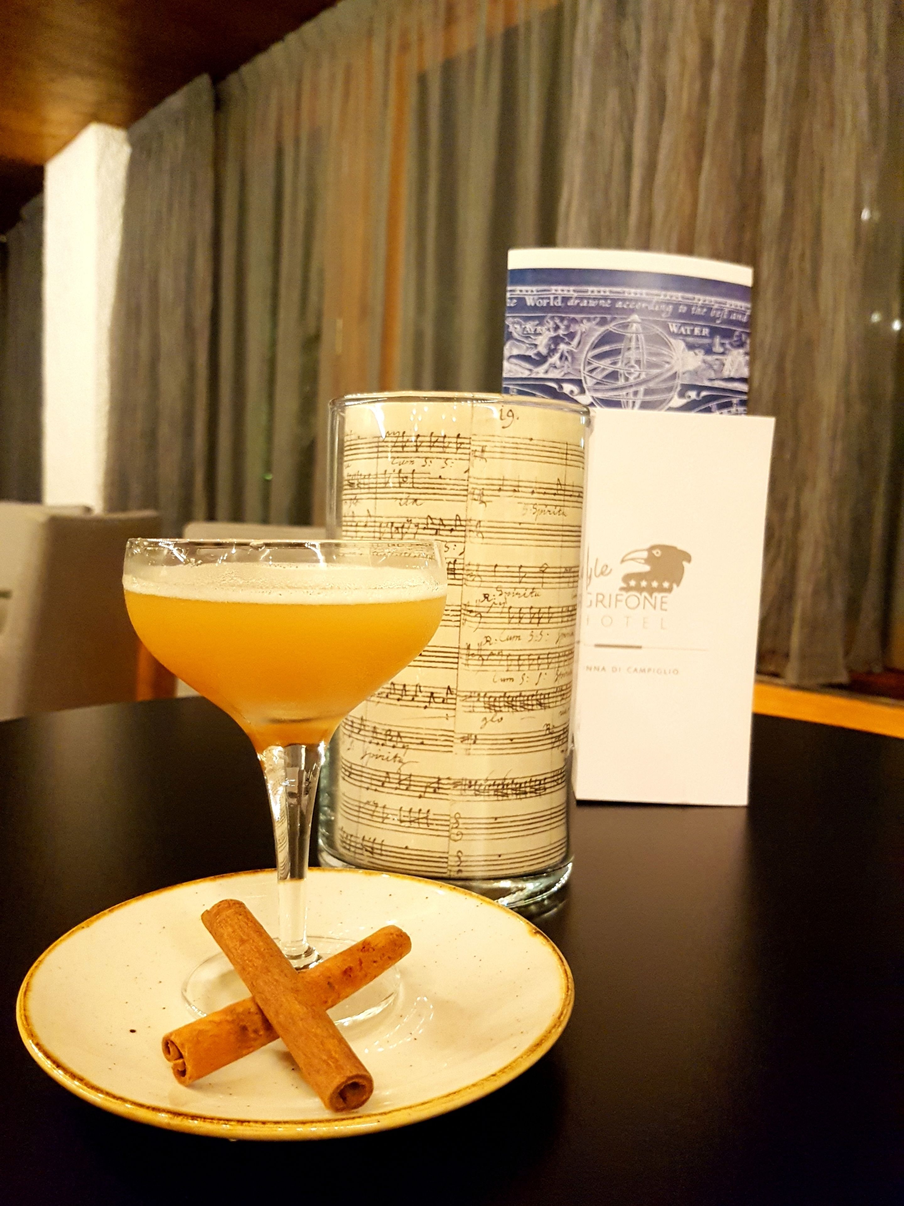 A cocktail glass with a cinnamon stick on a plate, a decorative candle, and a hotel brochure on a table.