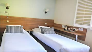 Una habitación de hotel con dos camas individuales, cada una con un cojín a rayas, un cabecero de madera y una mesita de noche con una lámpara y una bandeja de tazas de café.