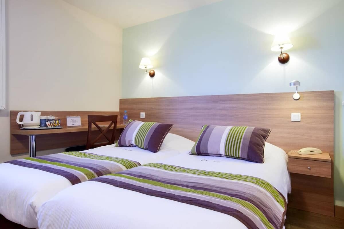 Ein Hotelzimmer mit zwei Betten, einem Schreibtisch und zwei Wandleuchten.