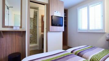 Une chambre avec deux lits, une télévision, un miroir et une fenêtre avec des stores.