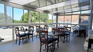 A restaurant with large windows, wooden tables, and chairs. - Brit Hotel Le 940 Le Touquet – Etaples (Etaples)