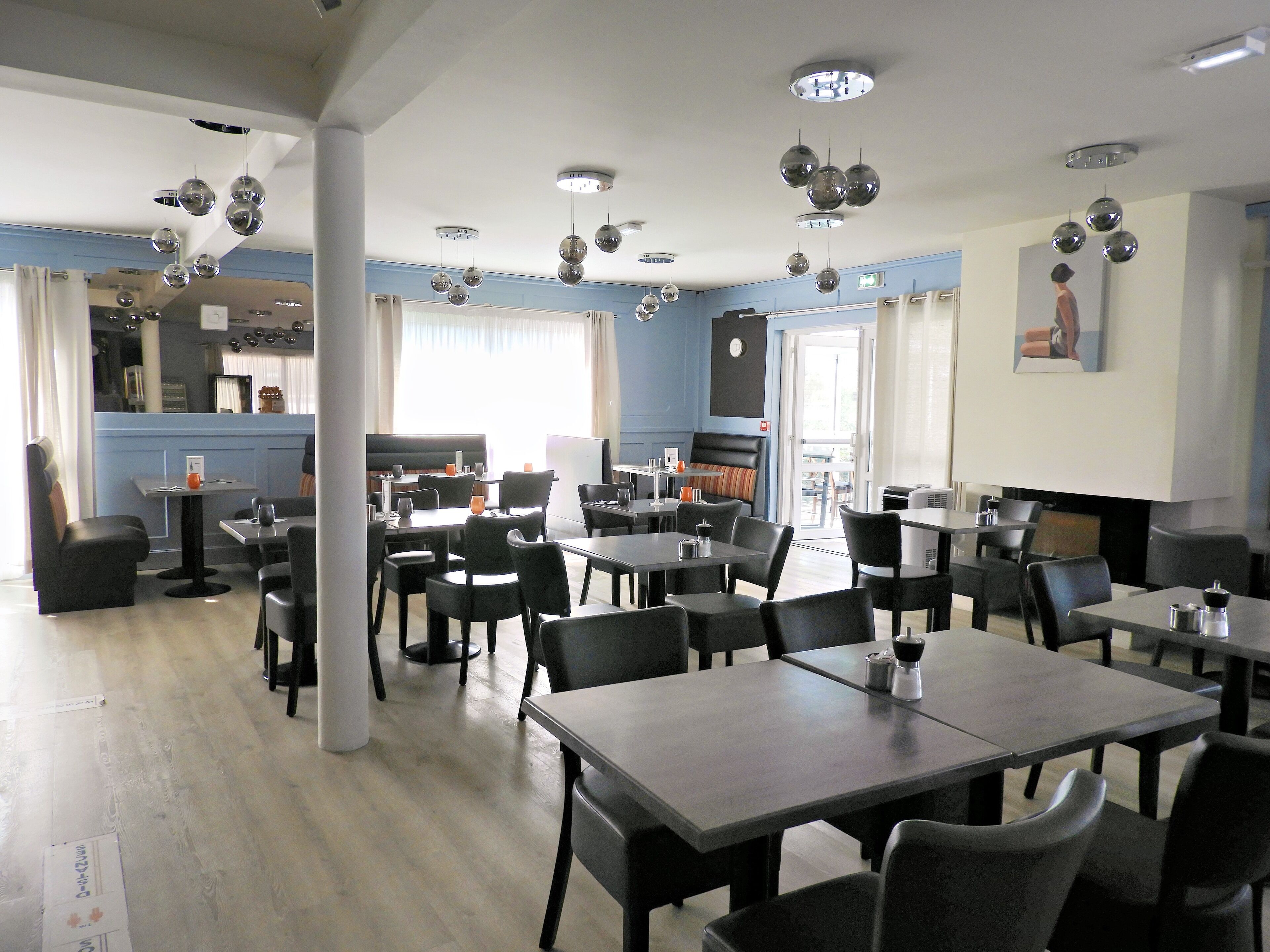 Un restaurant moderne doté de nombreuses tables et chaises, d’un bar et d’une grande fenêtre laissant entrer la lumière naturelle.