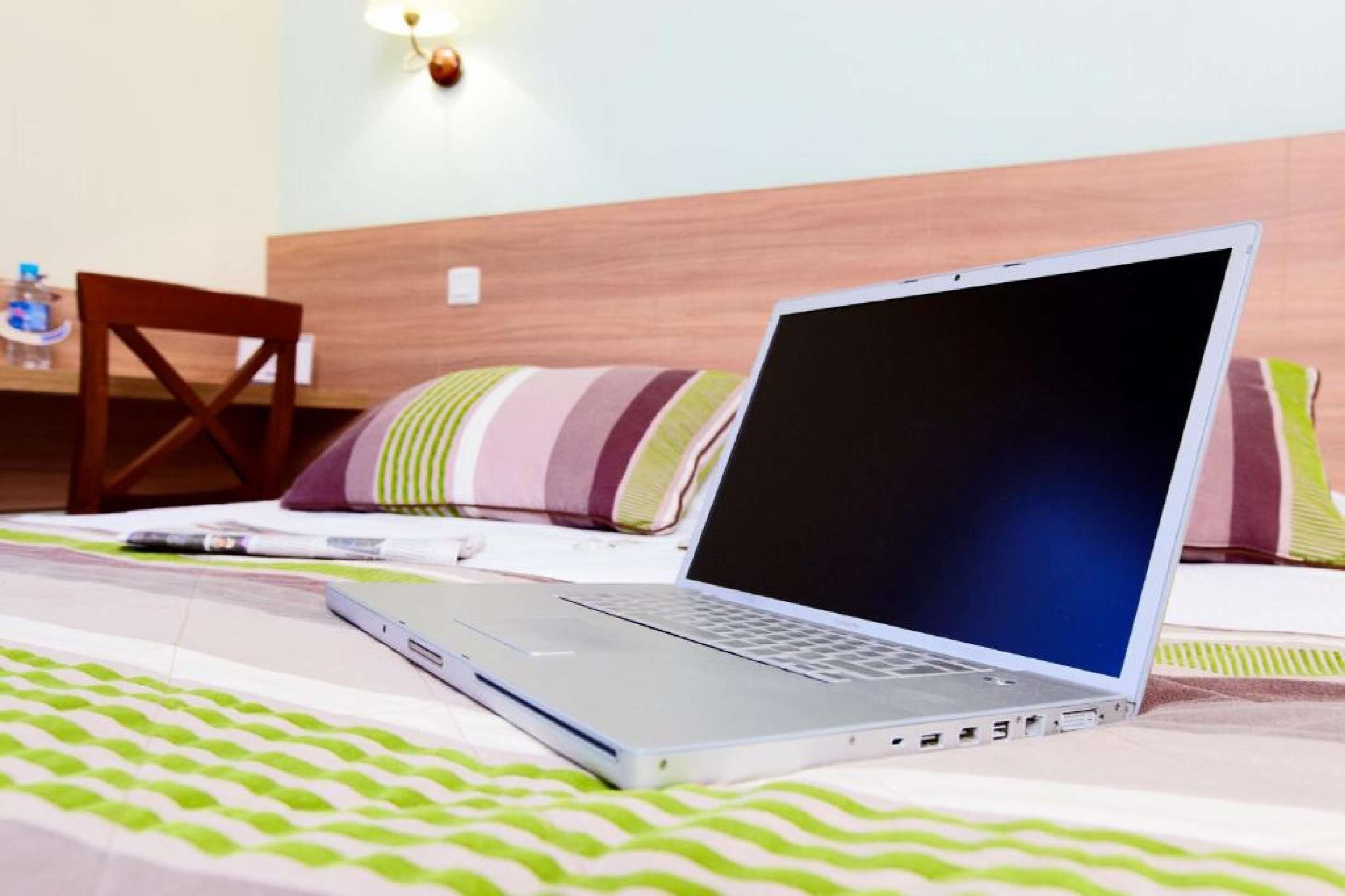 A laptop on a bed with a striped pillow and a water bottle on a table.
