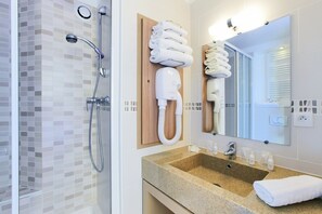 Een moderne badkamer met een glazen douche, een houten handdoekrek, een grote spiegel en een granieten wastafel.