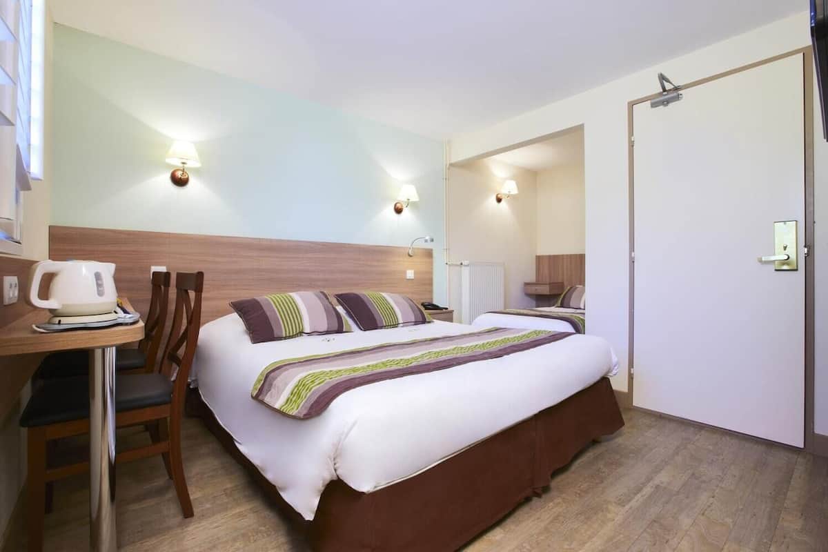 Ein Hotelzimmer mit Bett, Nachttisch, Sessel und Schreibtisch mit Wasserkocher.