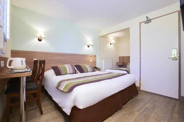 Een hotelkamer met een bed, nachtkastje, stoel en een bureau met waterkoker.