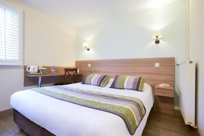 Een hotelkamer met een bed, nachtkastje, lamp en een radiator.
