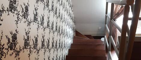 A wooden staircase with a patterned wallpaper on the left wall.