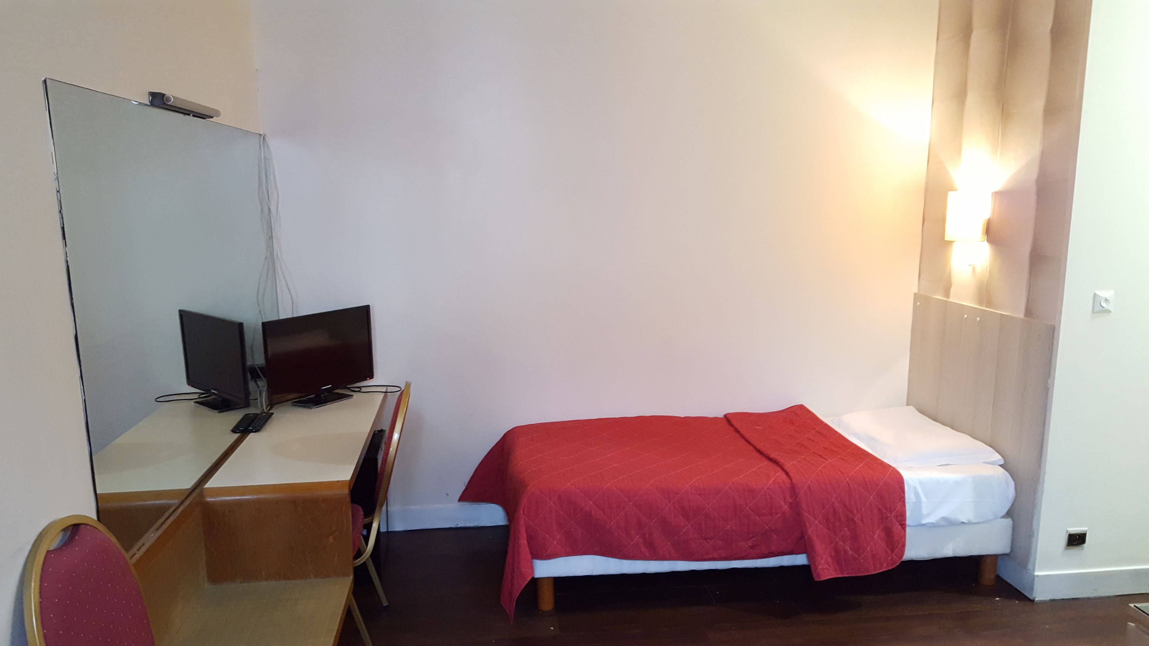 Ein kleines Zimmer mit einem Bett, einem Schreibtisch mit Computer und einem Spiegel.