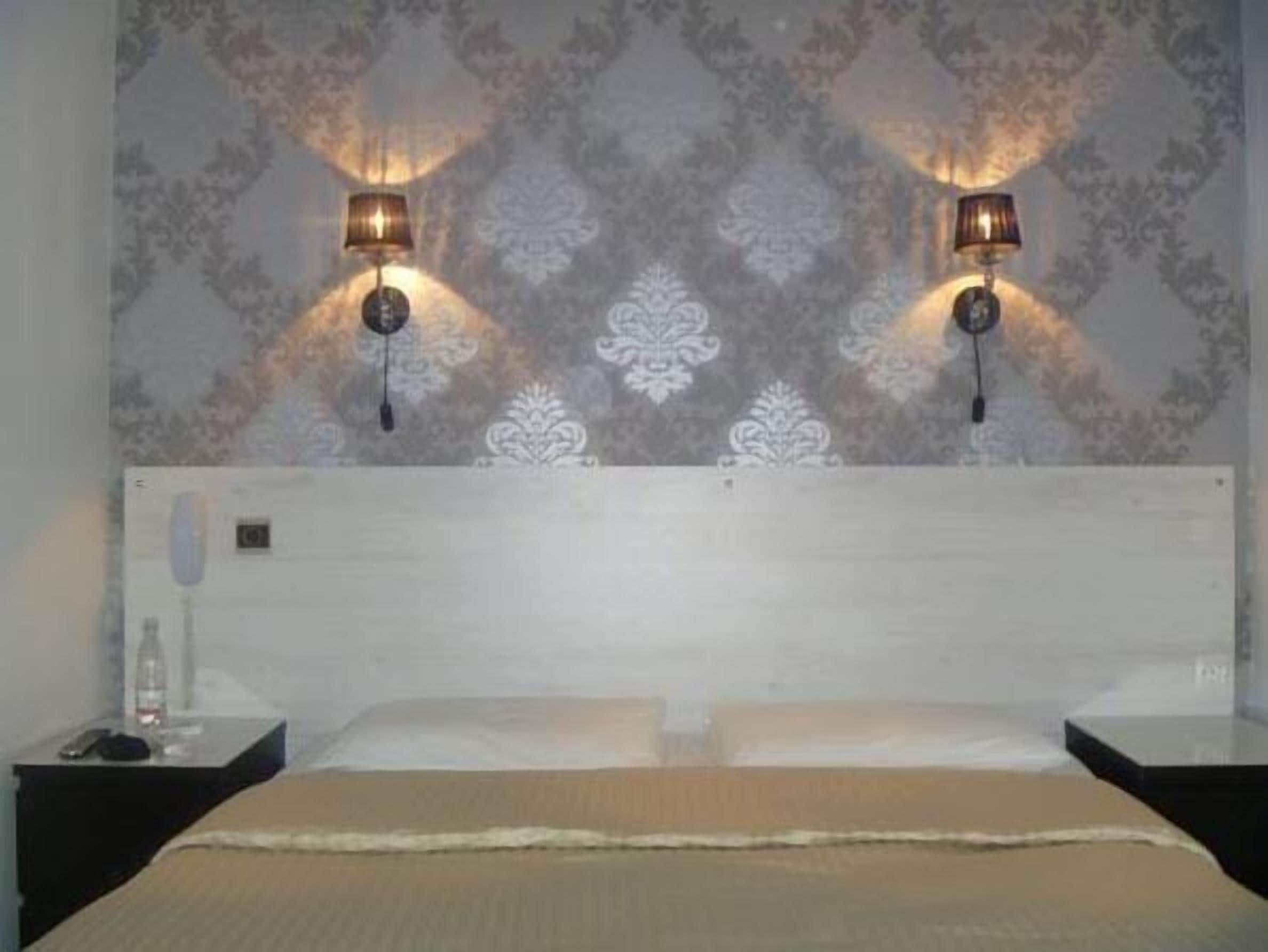 Cama doble con cabecera de madera, dos mesitas de noche y lámparas fijadas a la pared.