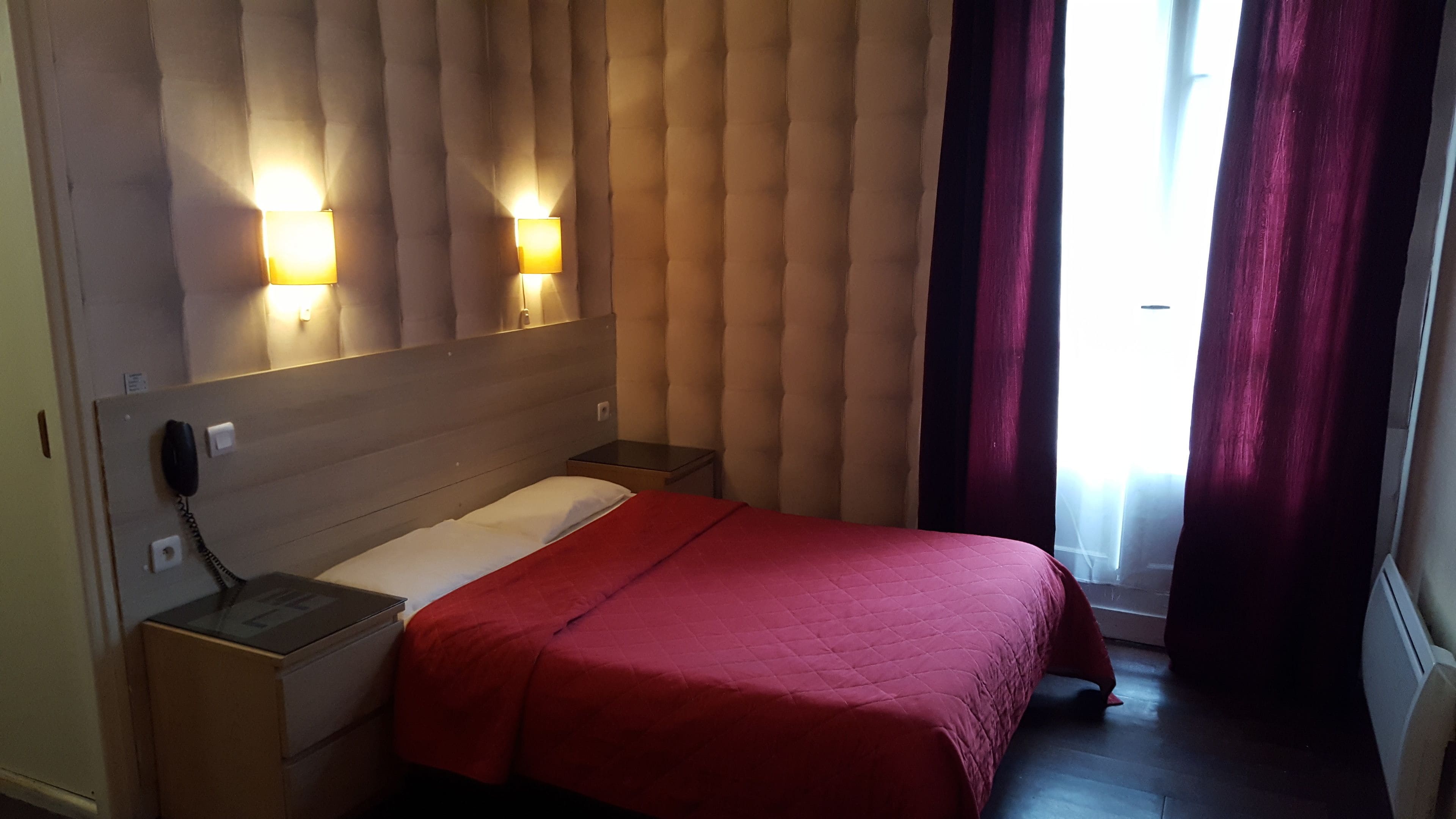 A hotel room with a bed, a nightstand, a telephone, and two wall-mounted lamps.