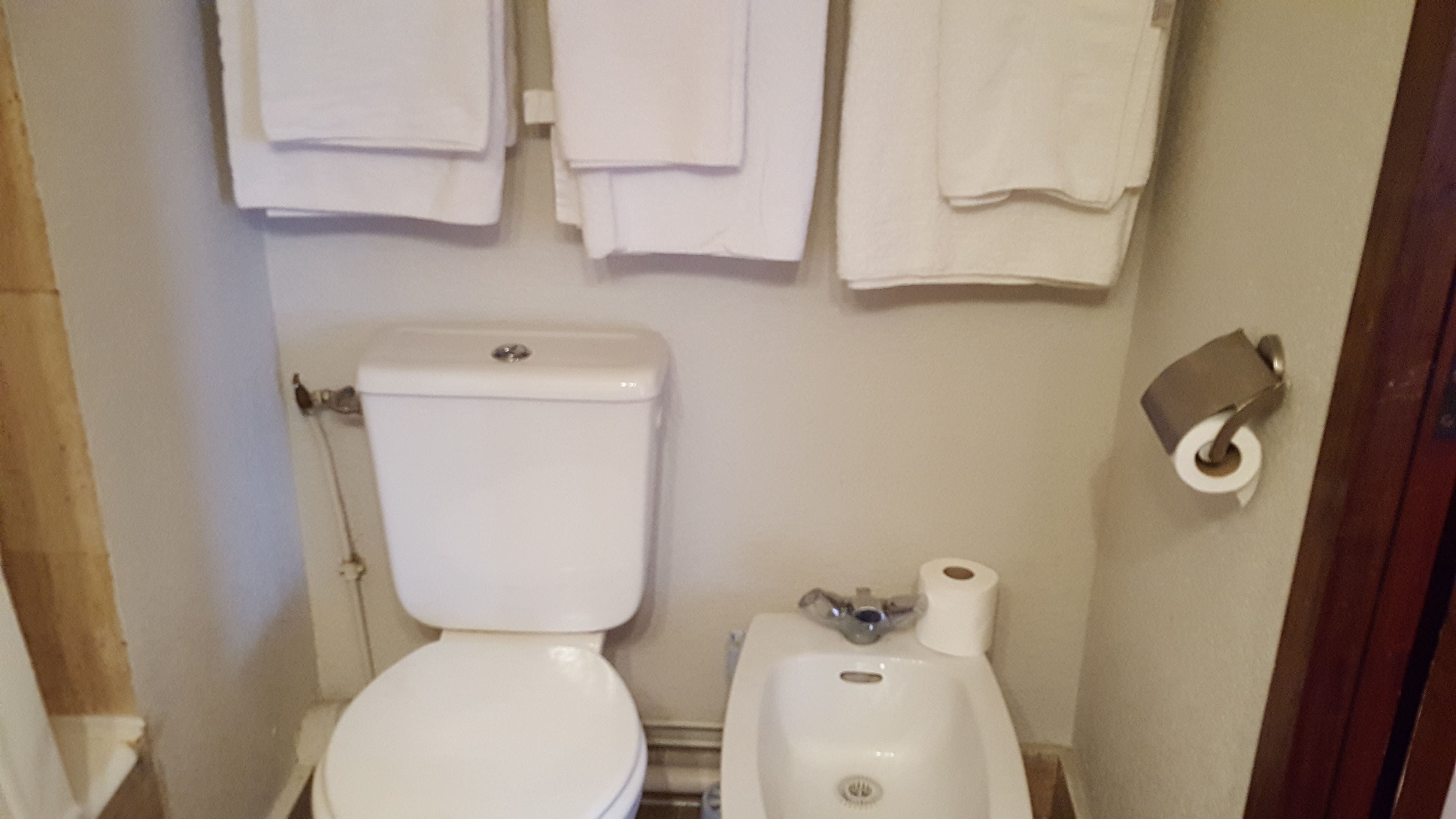 A small bathroom with a toilet, sink, and a towel rack with several towels.