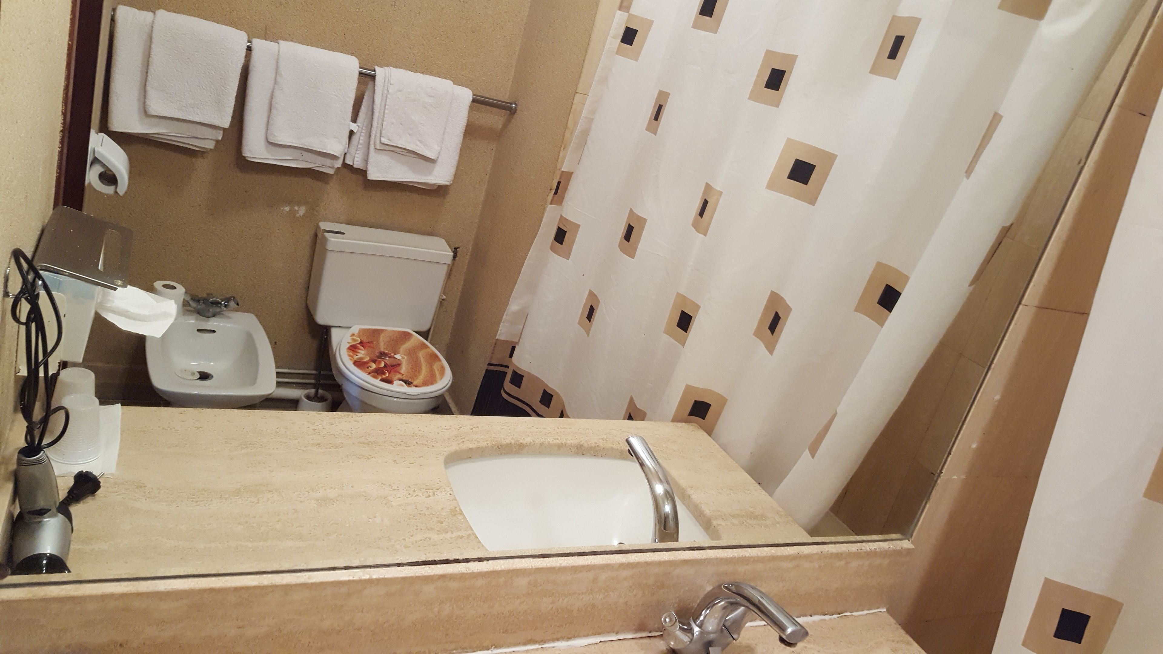 A bathroom with a sink, mirror, toilet, and shower curtain.