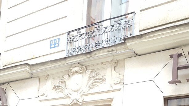 A building entrance with a wooden door, a metal gate, and a balcony with a railing. - Hôtel Media (Paris)