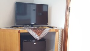 A compact room with a wooden desk, a black refrigerator, and a television on top. - Hôtel Media (Paris)