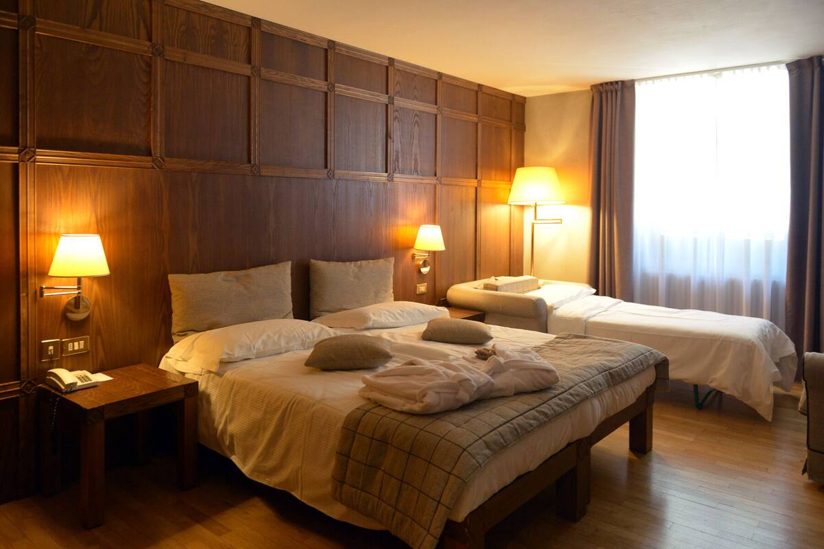 A hotel room with two beds, wooden paneling on the walls, bedside lamps, a wooden floor, and a window with curtains.