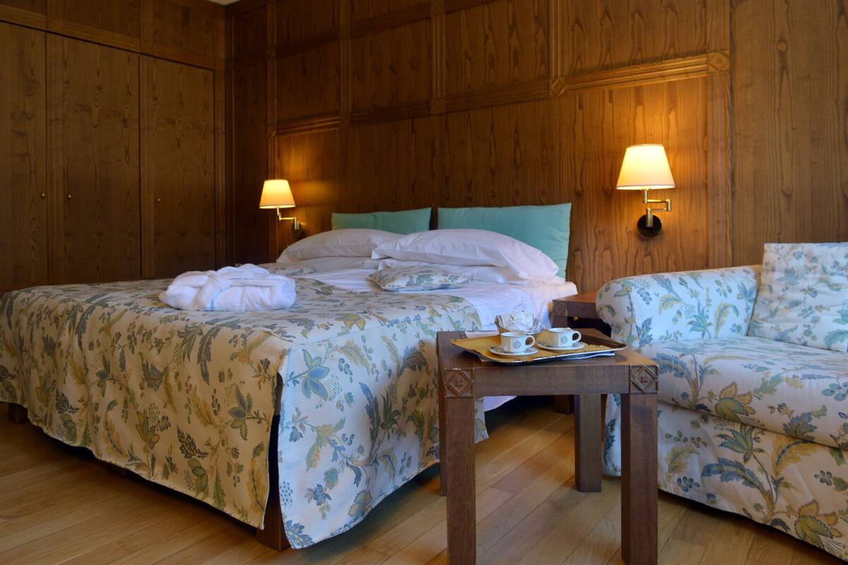 A hotel room with two beds, a sofa, and a small table with a tray of breakfast items.
