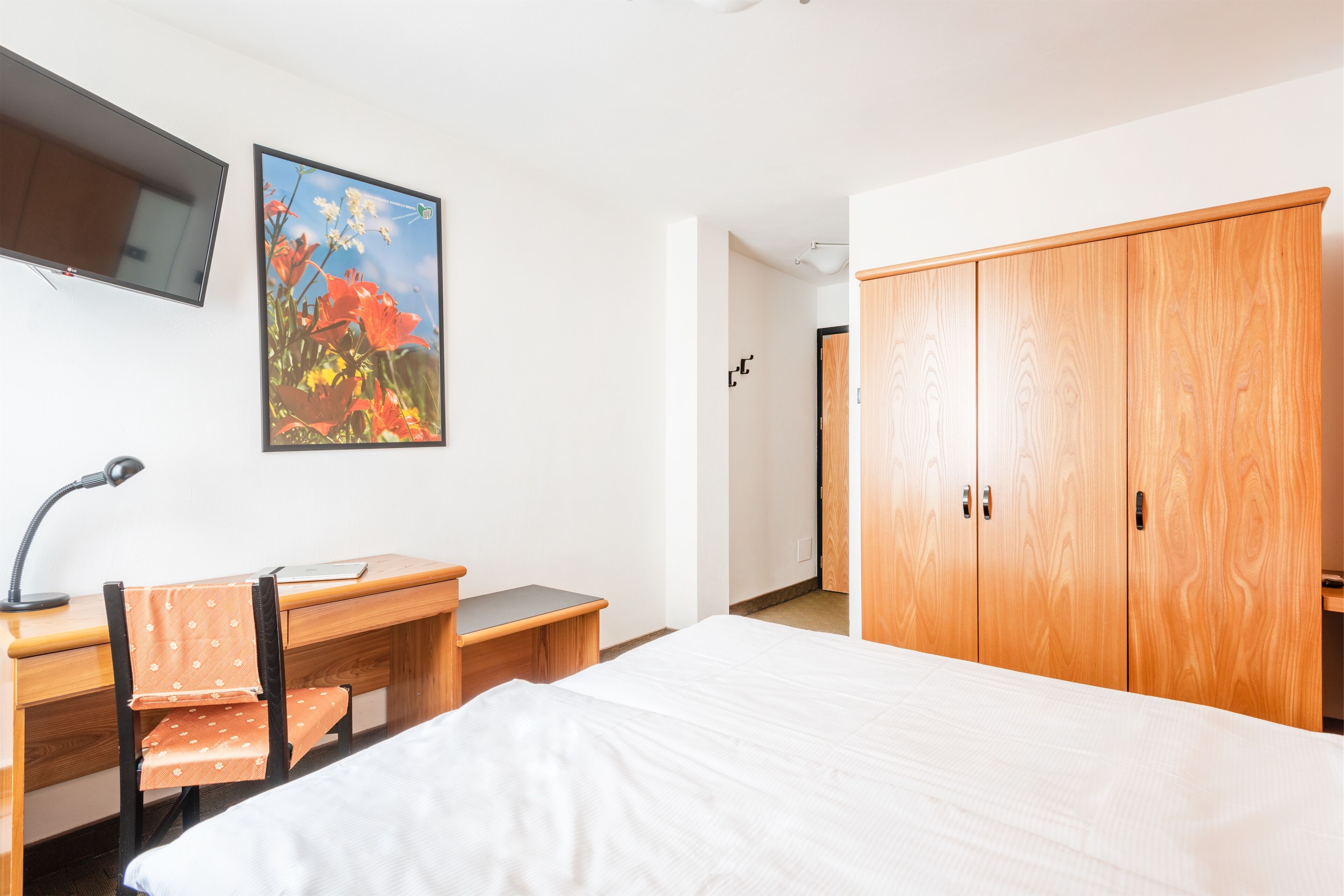 Un dormitorio con cama, escritorio con silla, televisor en la pared y armario.