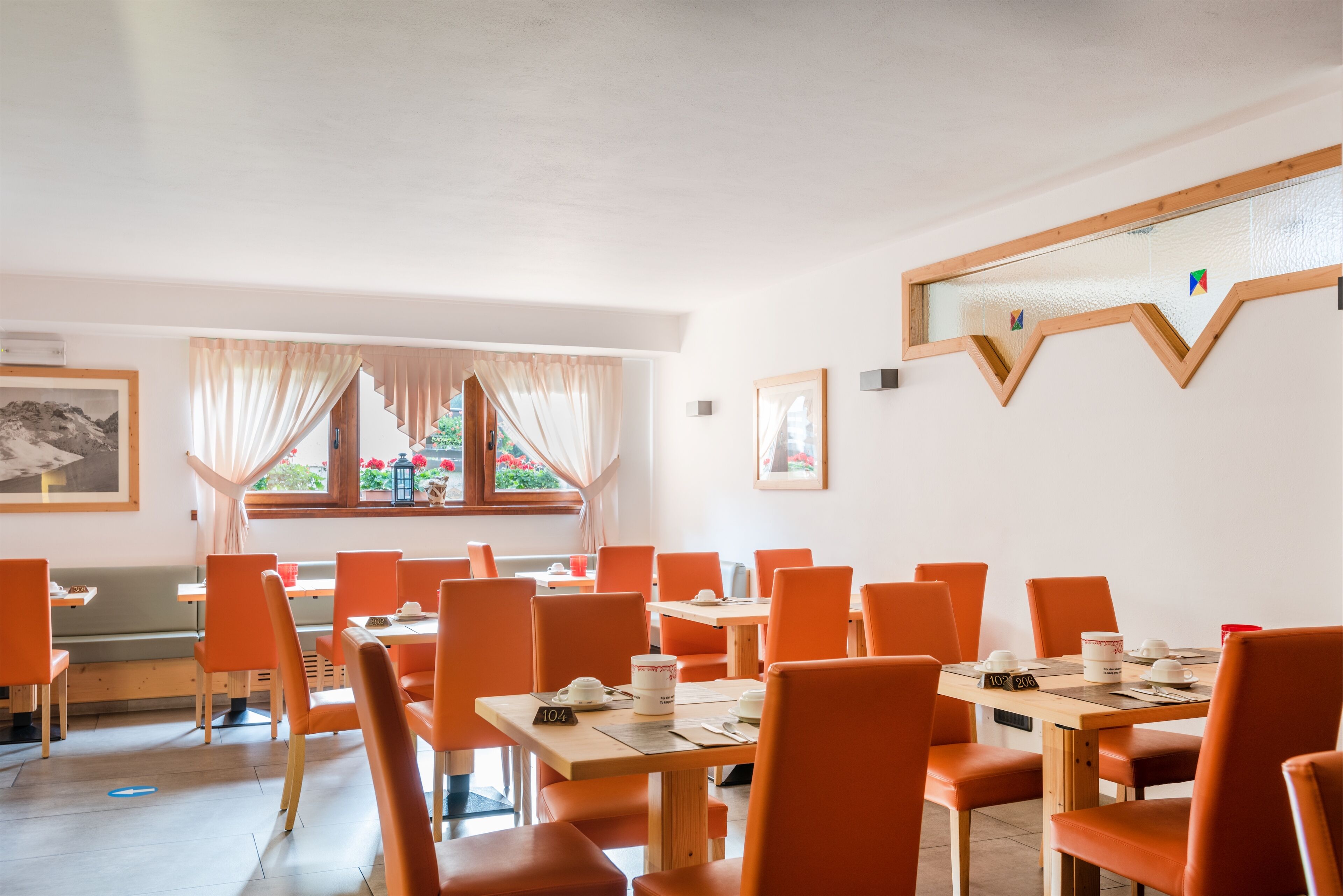 Un comedor con sillas y mesas naranjas, una ventana con cortinas y un cuadro en la pared.