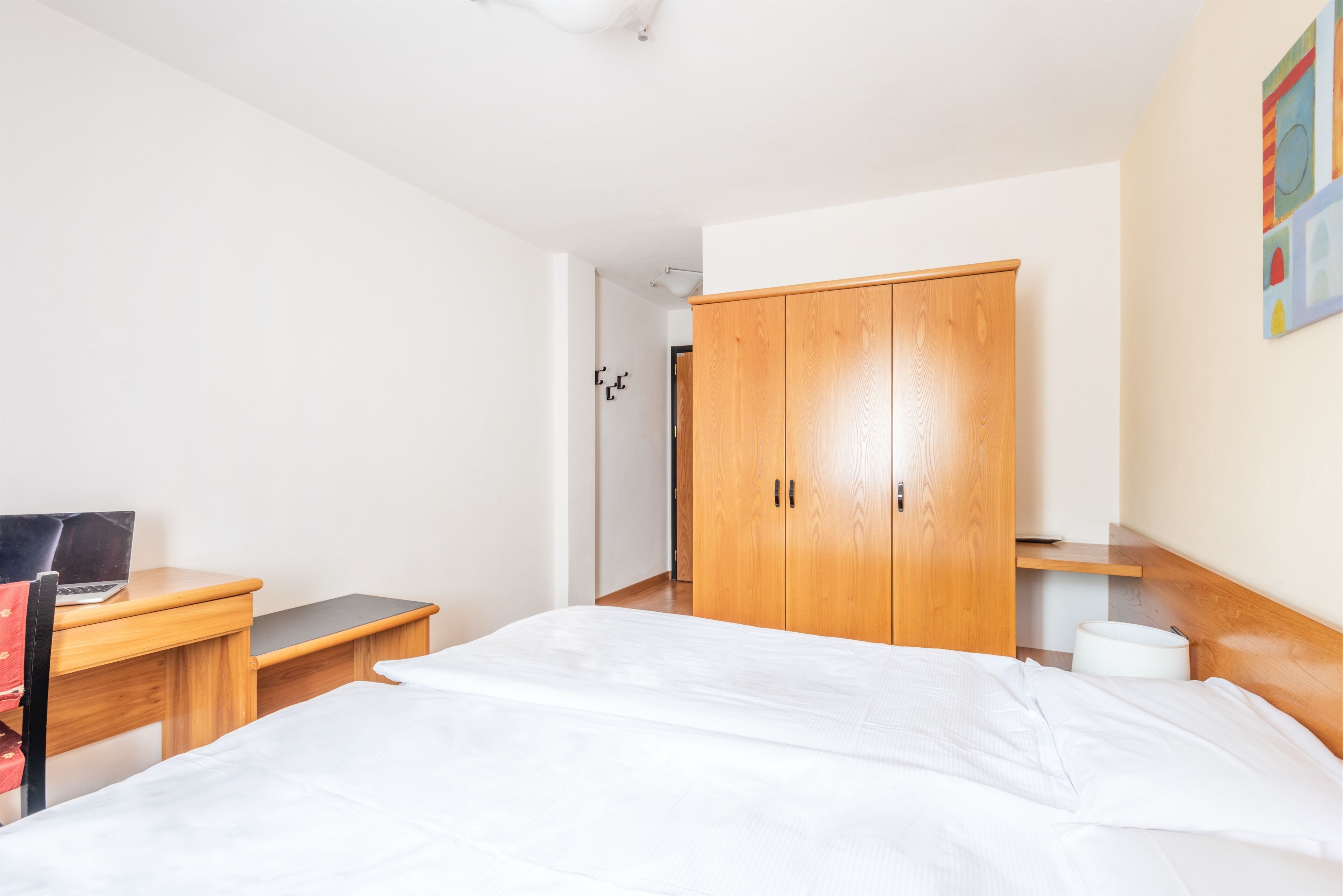 Ein Schlafzimmer mit Bett, Schreibtisch mit Laptop, Kleiderschrank und Toilette.