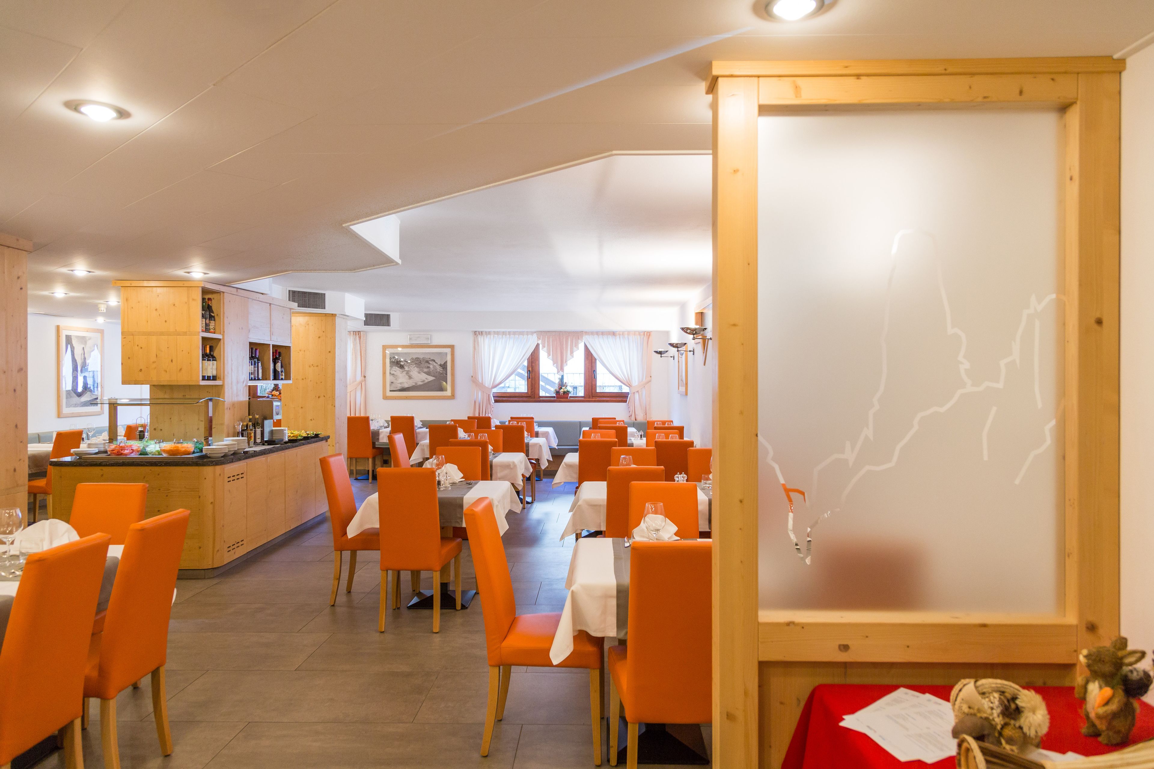 A restaurant with orange chairs and tables, wooden cabinets, and a large whiteboard with a map.