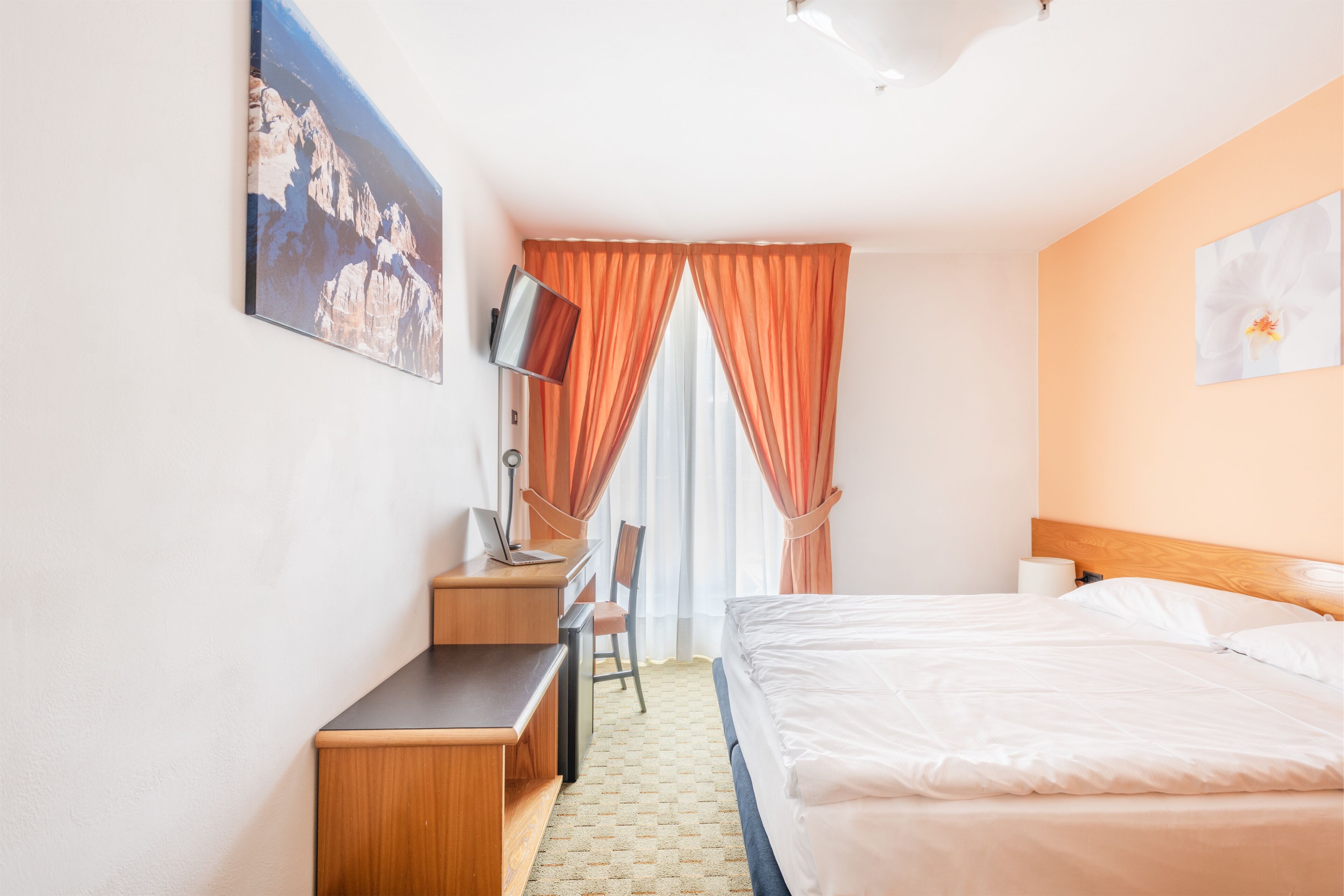 Une chambre d’hôtel avec deux lits, un bureau avec une chaise, une télévision et un tableau au mur.