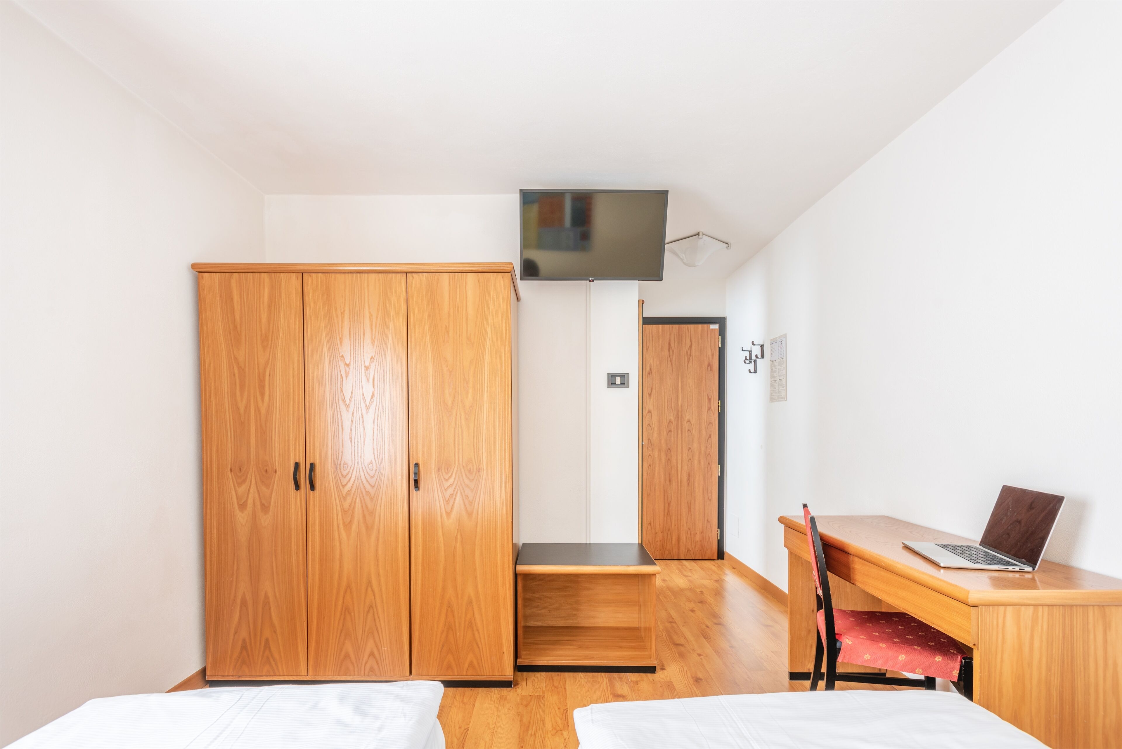 A bedroom with a wooden wardrobe, a desk with a laptop, and a bed.