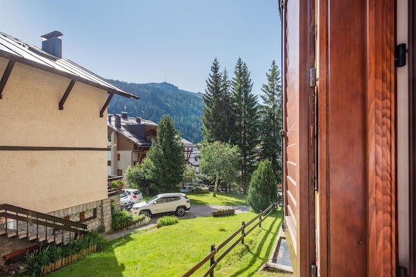 A view from a window overlooking a green lawn, a wooden fence, and a building with a sloped roof. - Hotel Alpina (Pinzolo)