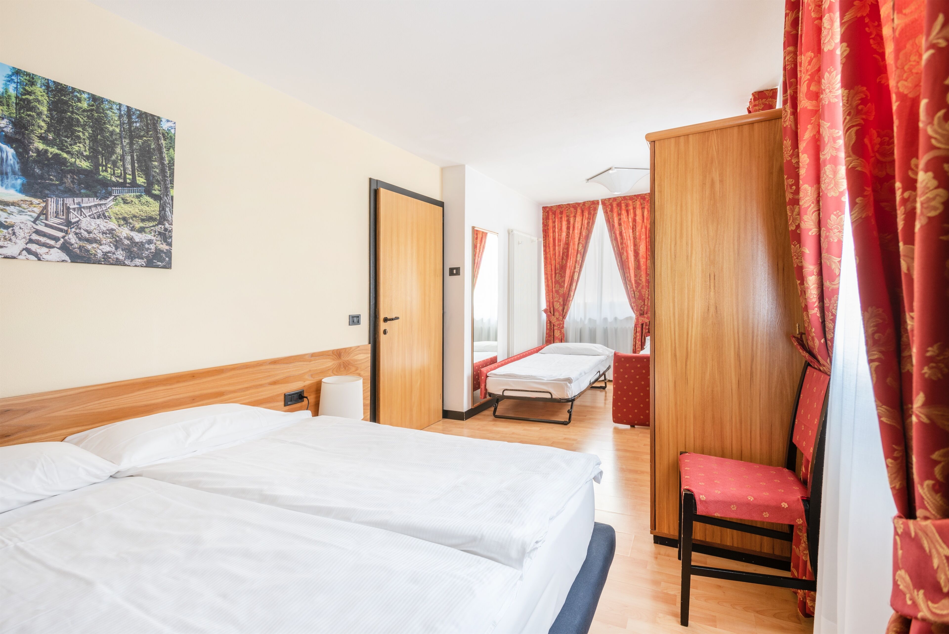 A hotel room with two beds, a wooden headboard, a red chair, and a painting of a waterfall.