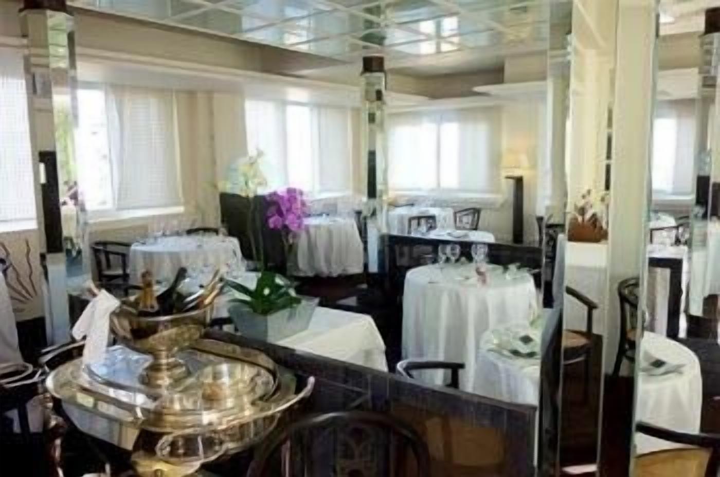 Un comedor con mesas dispuestas para el servicio, una pieza decorativa en el centro y un ventanal que proporciona luz natural.