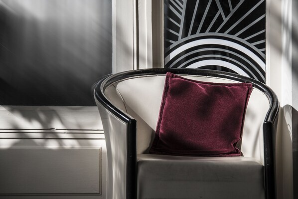 Una silla con estructura metálica y un cojín blanco, ubicada junto a una ventana con una celosía de metal decorativa.