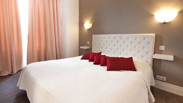 A neatly made bed with white bedding and red pillows, a tufted headboard, and wall-mounted light fixtures.