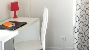 Un bureau blanc avec une lampe rouge, une chaise blanche et un rideau à motifs.