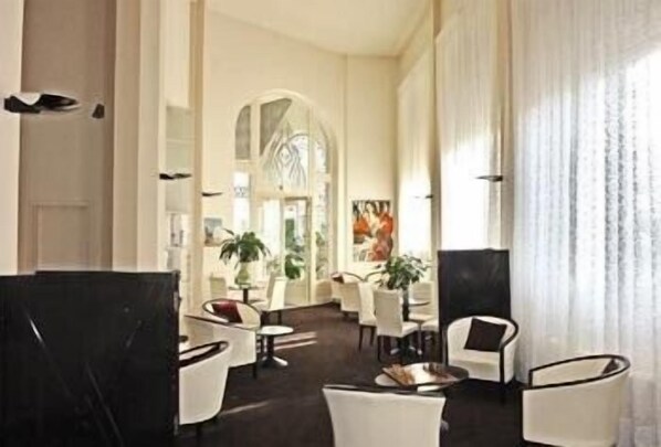 A spacious lobby with high ceilings, white furniture, and a large window with sheer curtains.
