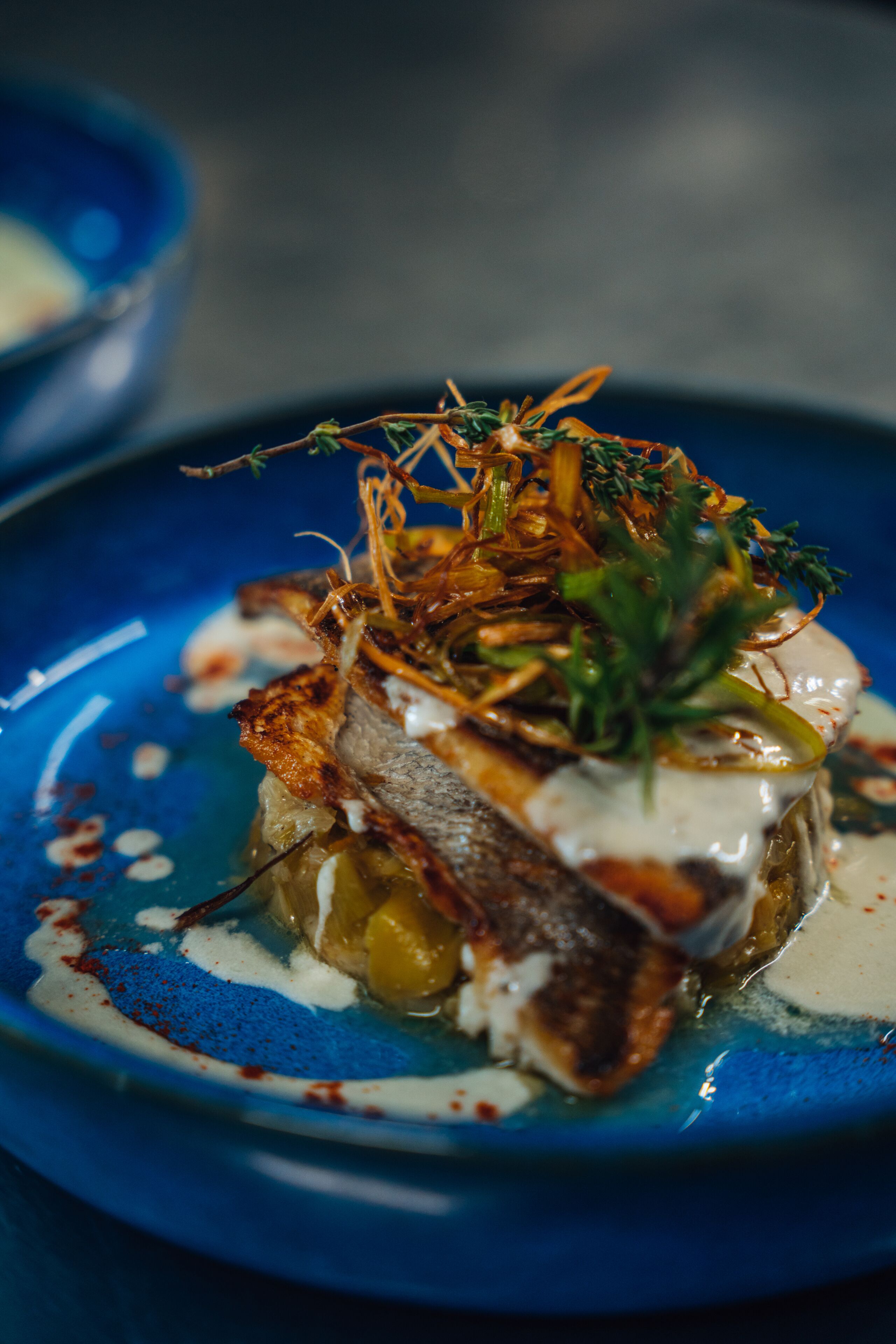 Un plato azul con un plato de pescado, adornado con hierbas y salsa.