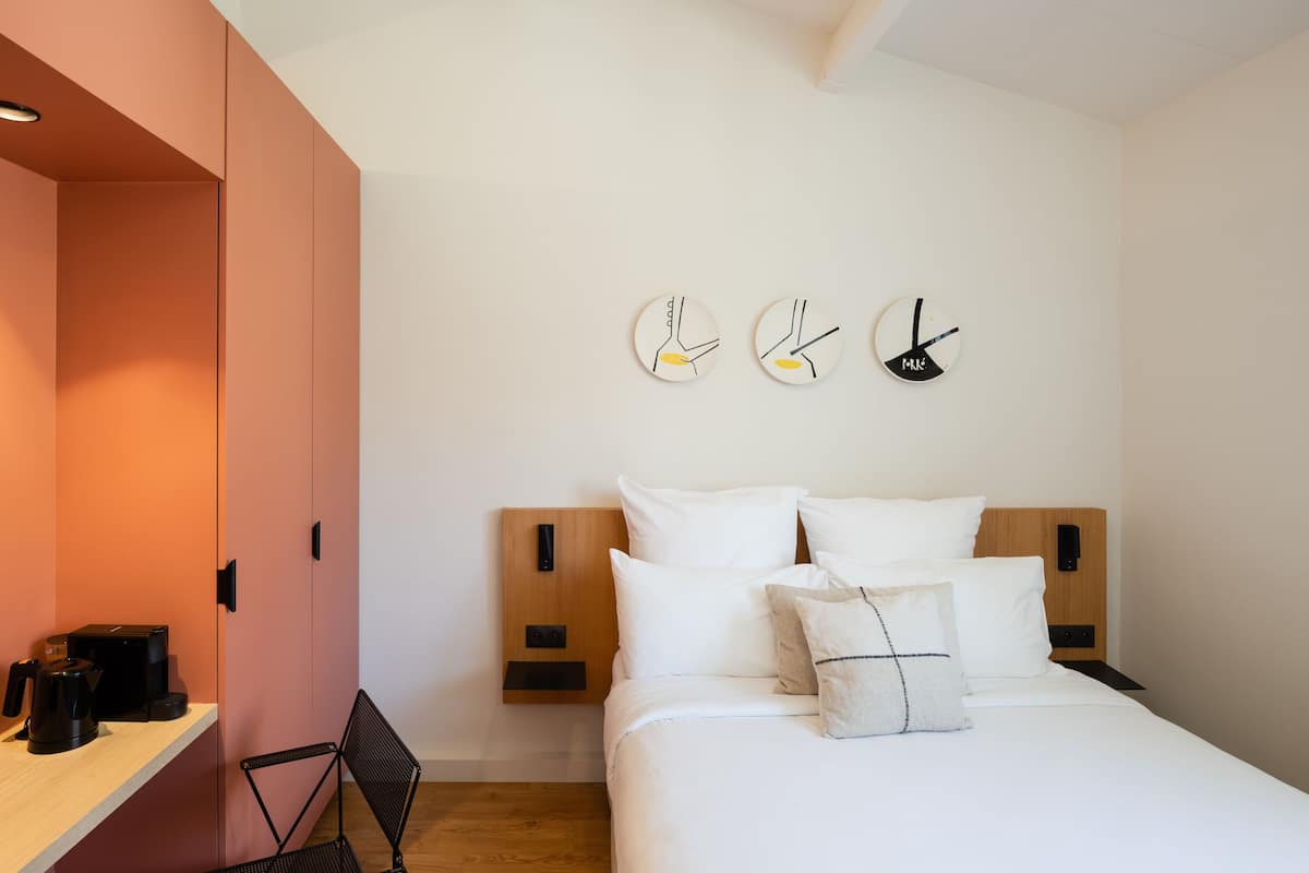A modern bedroom with a bed, bedside tables, and a wall-mounted clock.