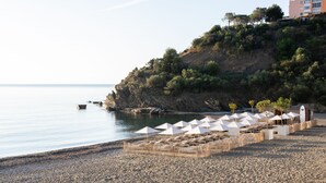Una playa con sombrillas y sillas de descanso, un acantilado rocoso y un edificio al fondo.