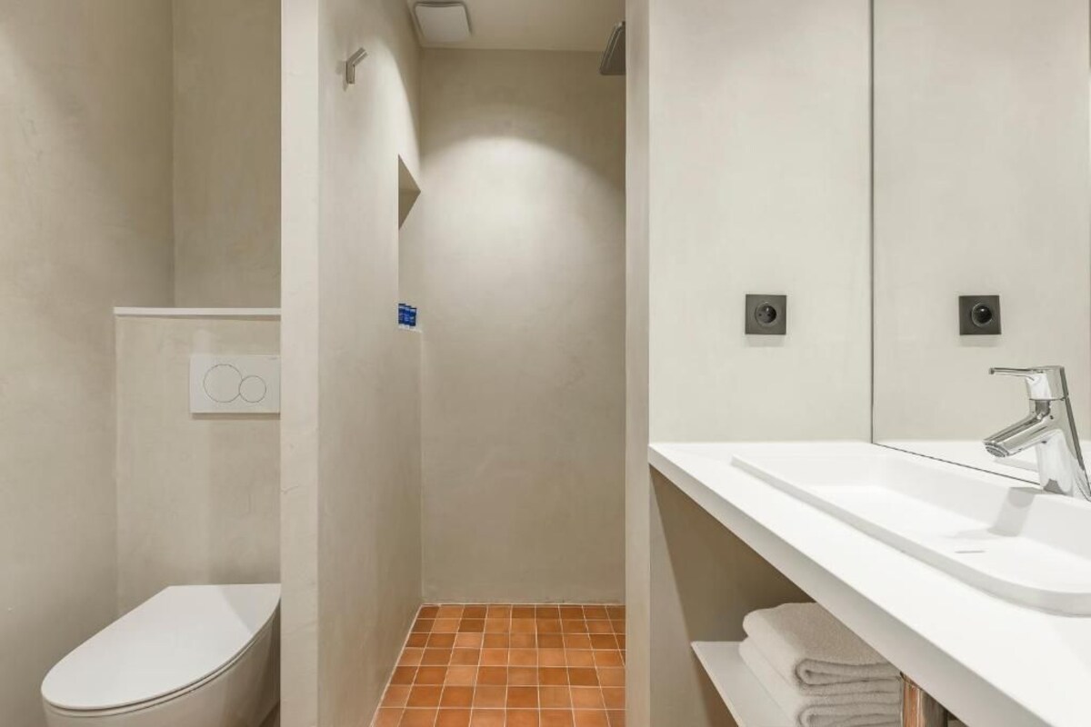 A modern bathroom with a white toilet, a shower area, and a sink with a mirror.