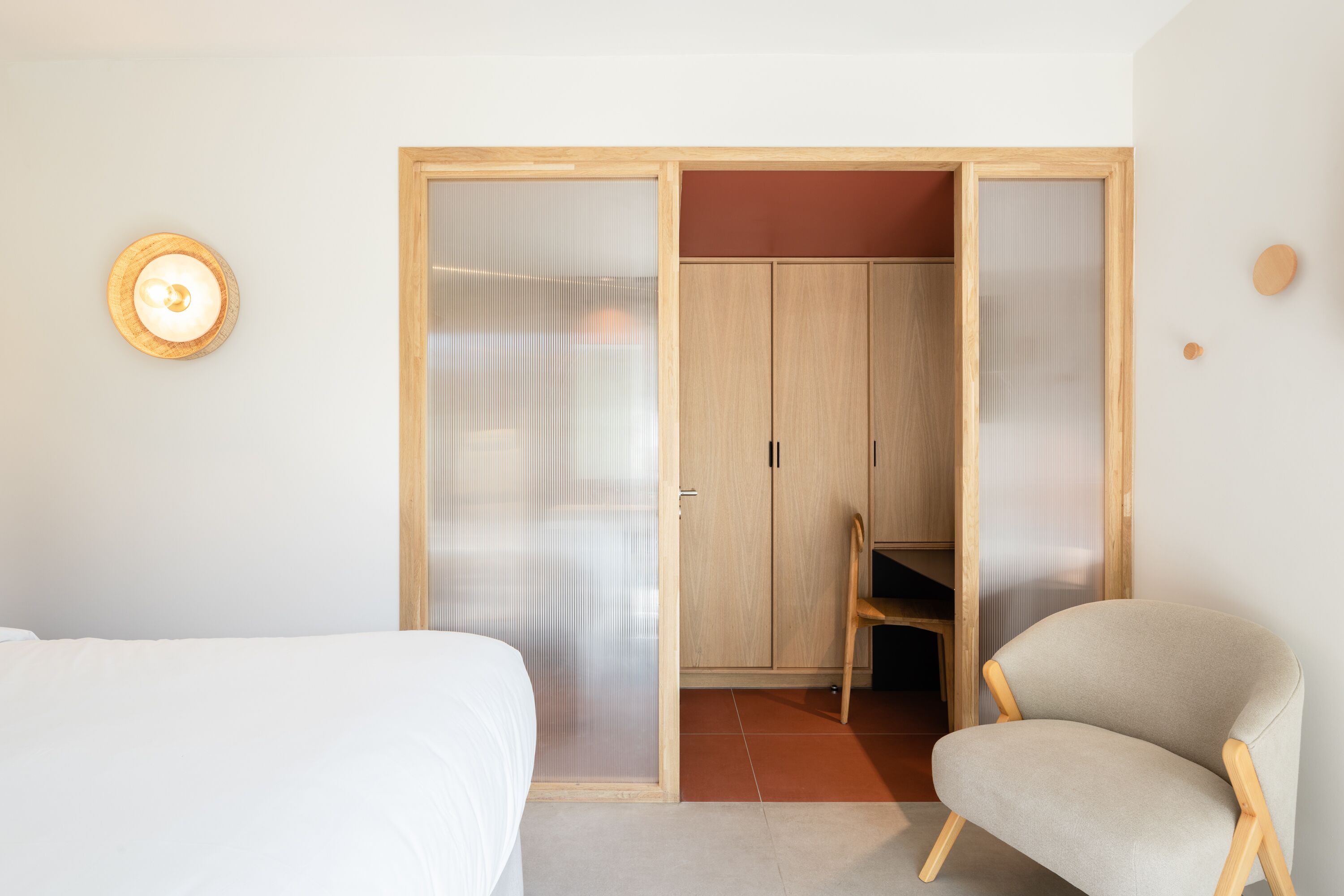 Une chambre à coucher comprenant un lit, une chaise, une armoire et un luminaire fixé au mur.