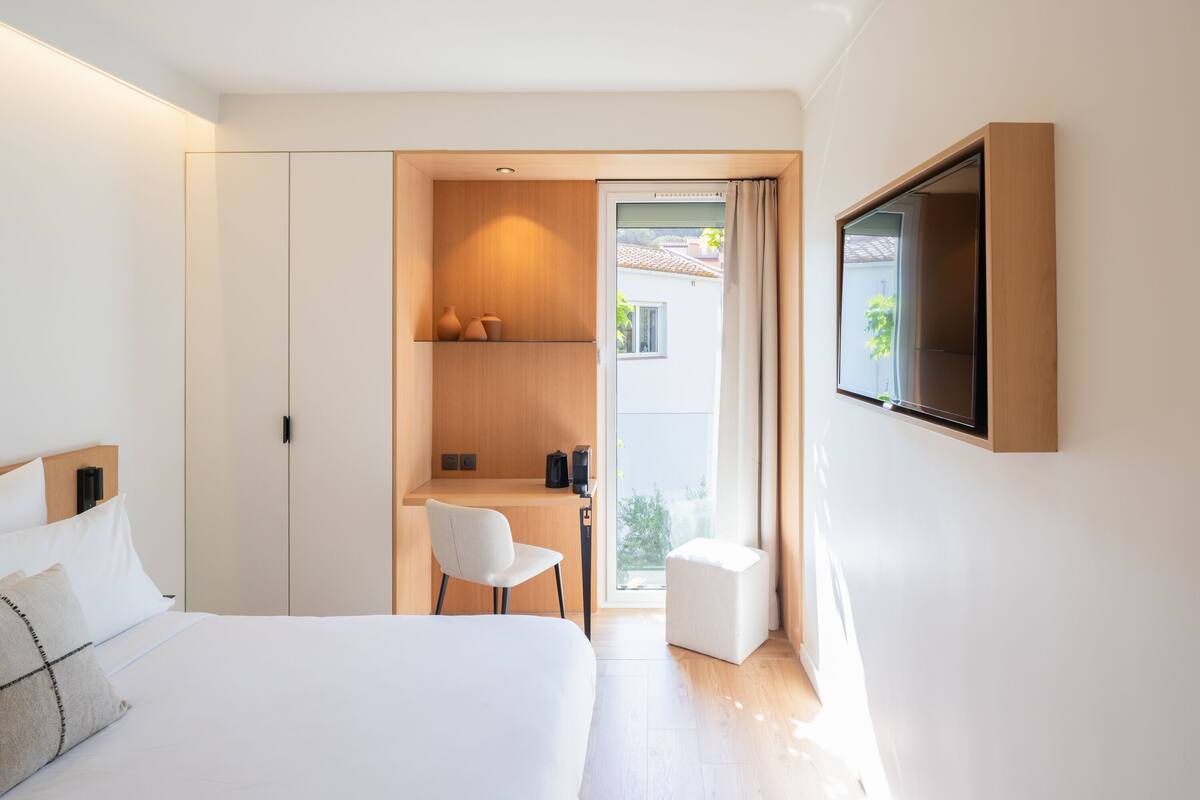 A modern hotel room with a bed, a desk, and a TV mounted on the wall.