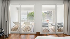 Una habitación de hotel moderna con suelo de madera, una cama y un balcón con dos sillas y una mesa.