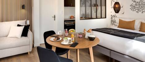 Un dormitorio moderno con una cama, una mesa de comedor con artículos para el desayuno, un sofá y una zona de cocina.