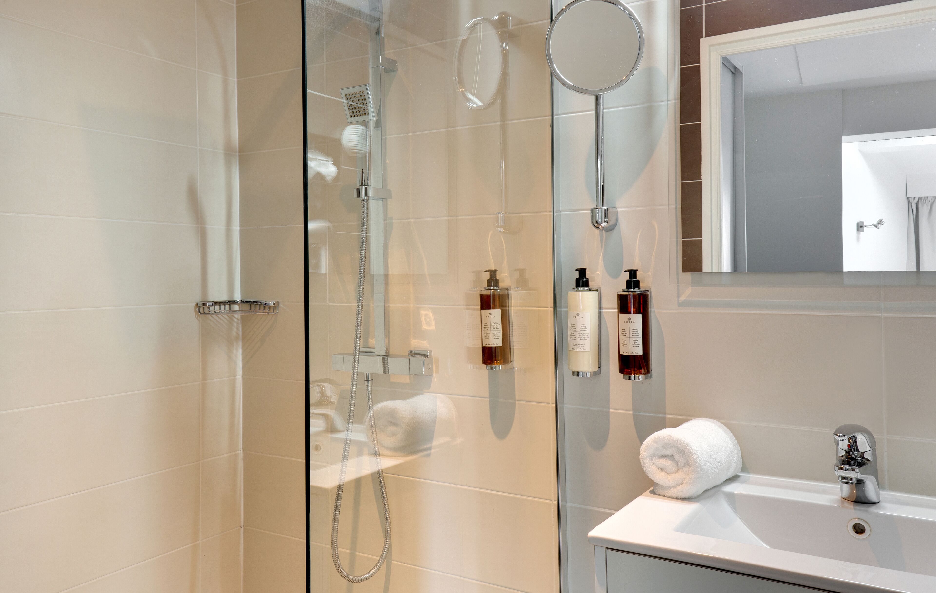 Een moderne badkamer met een douchecabine van glas, een witte wastafel en toiletartikelen aan de muur.