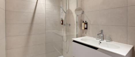 Une salle de bain moderne avec une douche à parois de verre, un lavabo blanc et deux bouteilles de shampoing accrochées au mur.