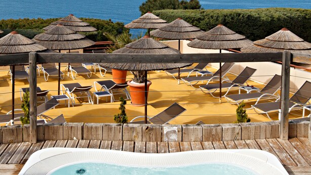 Un jacuzzi con vista despejada al mar y sillones de descanso con sombrillas.