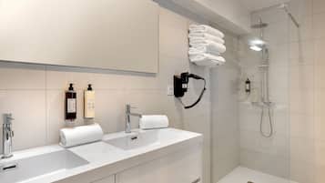 Une salle de bain moderne avec un grand miroir, deux lavabos, une douche et des serviettes soigneusement pliées.