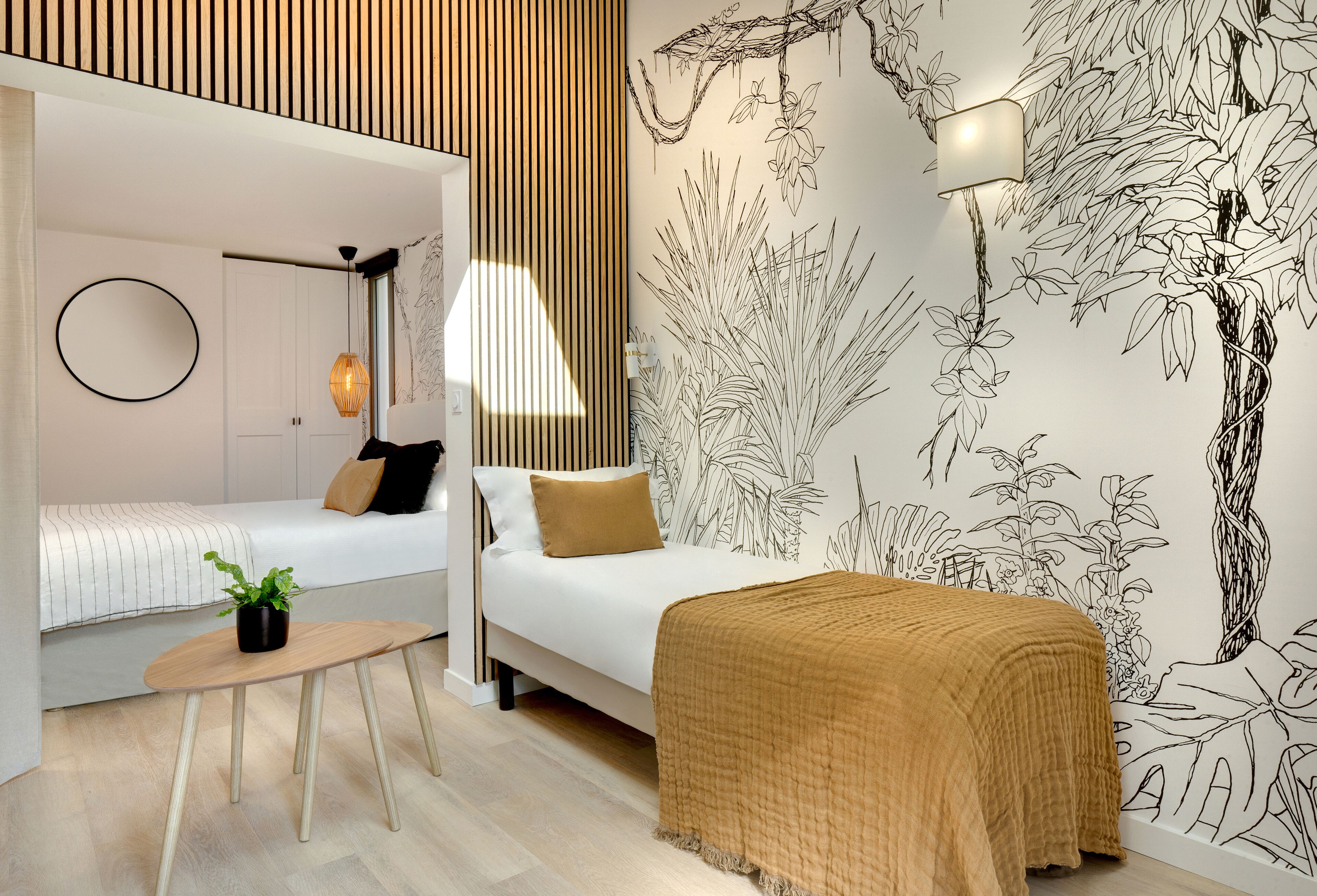 A modern bedroom with two beds, a small table with a plant, and a wall mural.